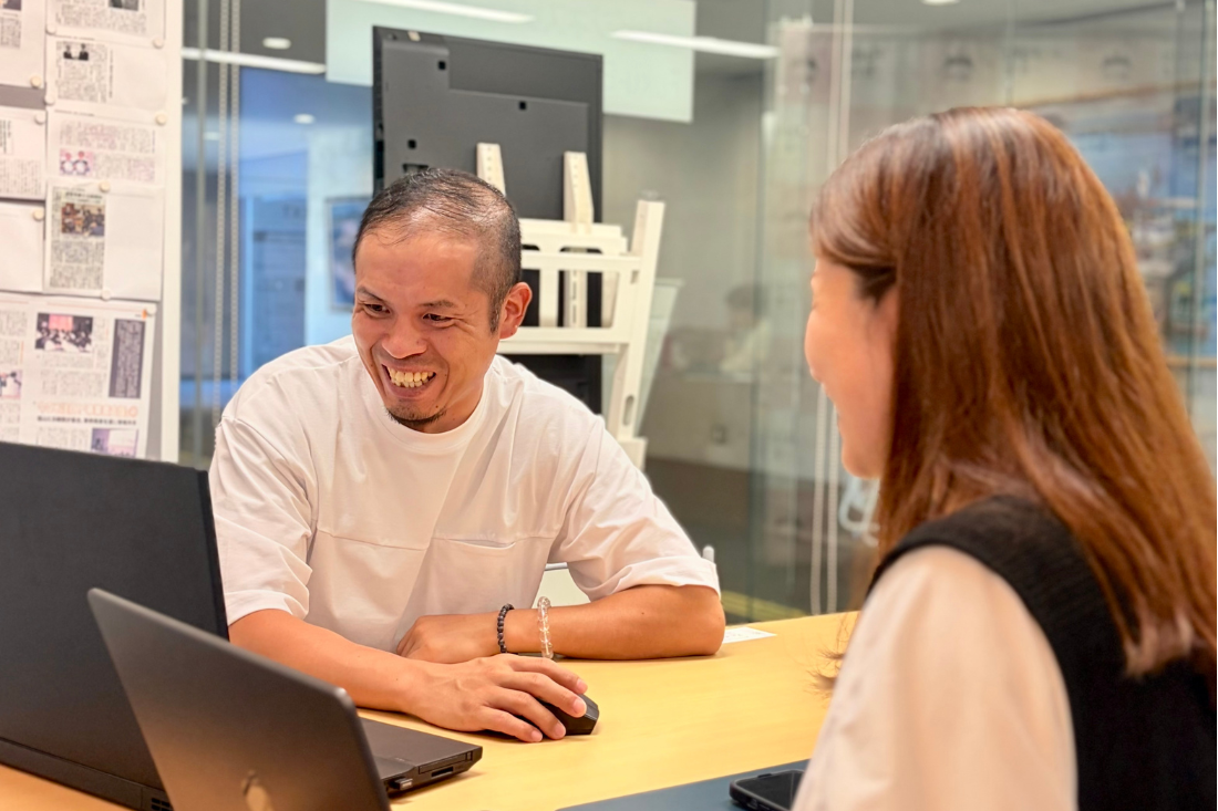 Man and woman at a desk in an office, smiling during a laptop-assisted consultation.